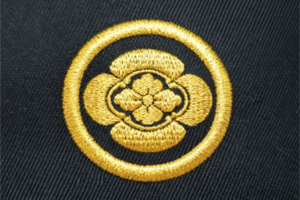 黒地の生地に金糸で円形の家紋を刺繍した高級感のある刺繍加工