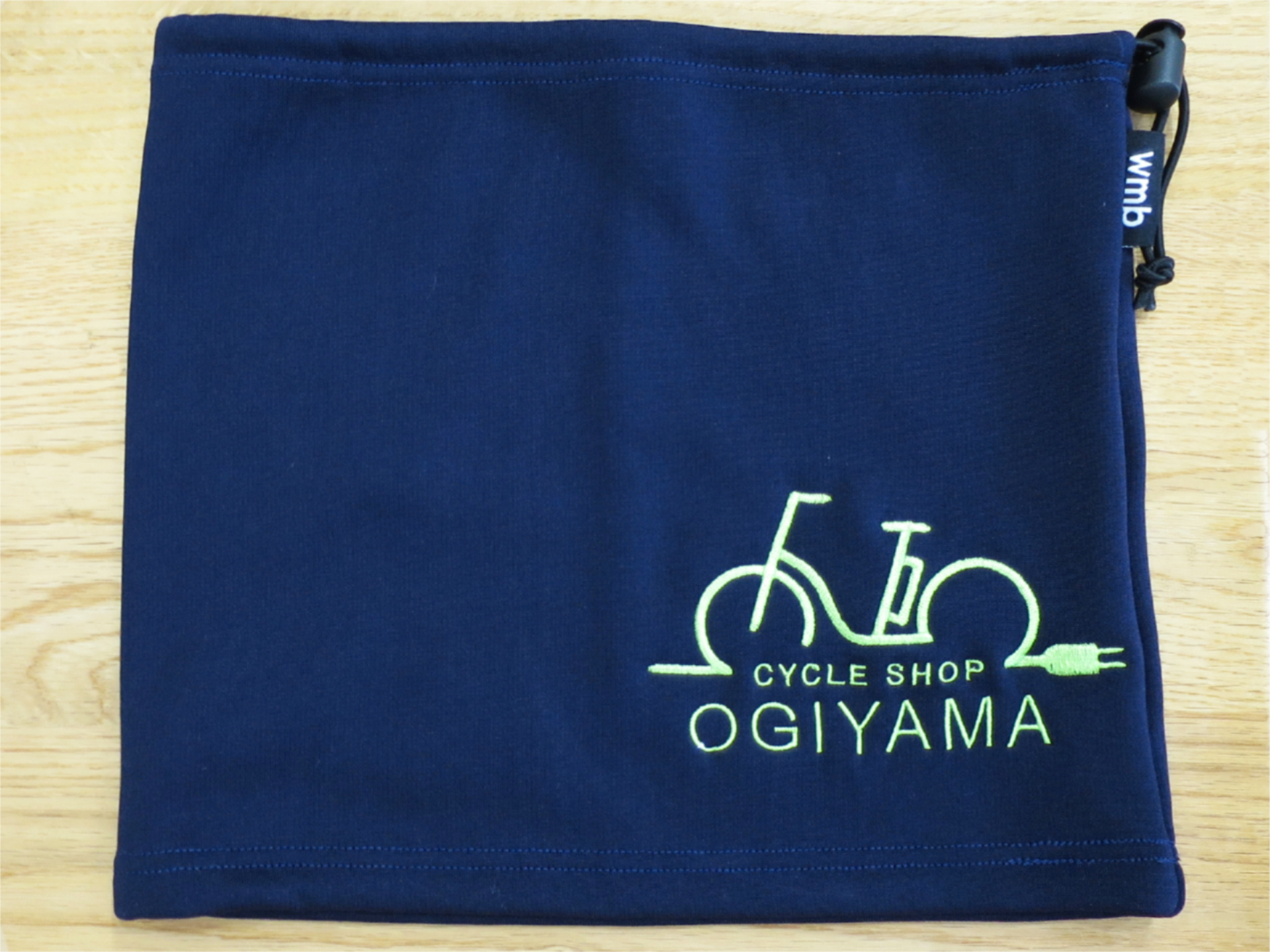 ネイビーのネックウォーマーに、サイクルショップOGIYAMAの自転車モチーフロゴを黄緑色の刺繍で入れたオリジナル刺繍実績