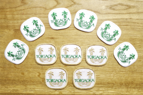 細かい文字入りロゴを刺繍したワッペン制作事例｜ゴールドとグリーンの2カラー展開