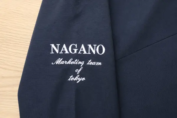 ネイビーのユニフォーム袖に「NAGANO Marketing team of tokyo」の文字を白糸で刺繍した社名・チーム名刺繍の制作事例