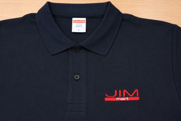 ネイビーのドライポロシャツに赤糸で「JIM mart」のロゴ刺繍を施したオリジナルユニフォーム制作事例。商品手配から刺繍加工までワンストップで対応した短納期ポロシャツ。
