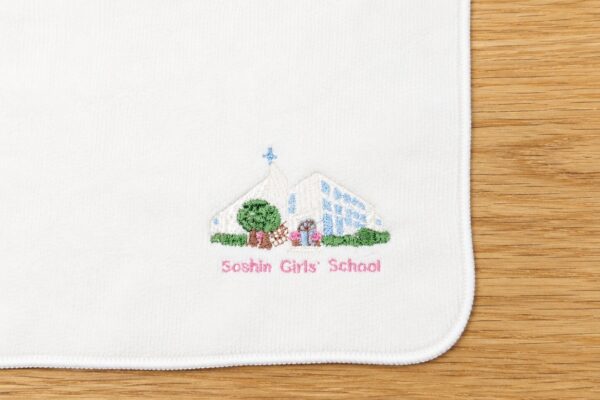 校舎のイラストと校名を刺繍したオリジナルハンドタオル。卒園記念や学校の記念品として制作。