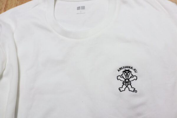 白いTシャツの胸元に、キャラクターと円弧状の文字を黒糸で刺繍したオリジナルデザイン刺繍の制作例