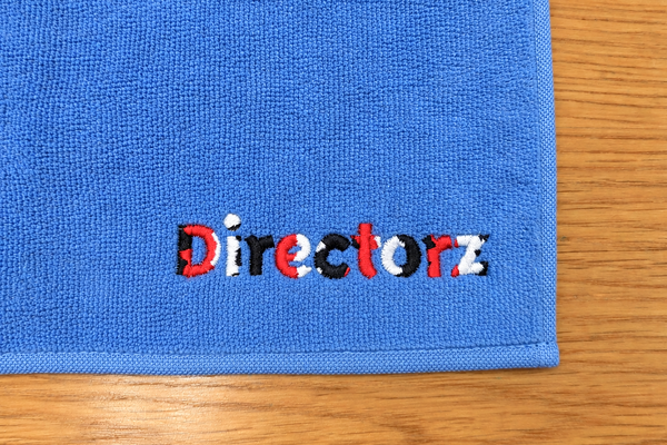 青のハンドタオルにDirectorzの文字を赤・黒・白で刺繍した販促品の制作事例