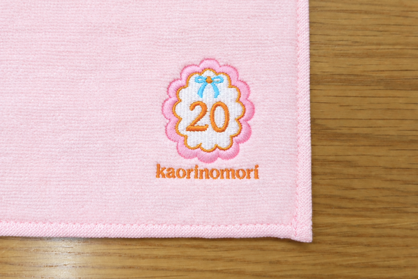 販促用ハンドタオルに20の花柄デザインとkaorinomoriの文字を多色刺繍した制作事例