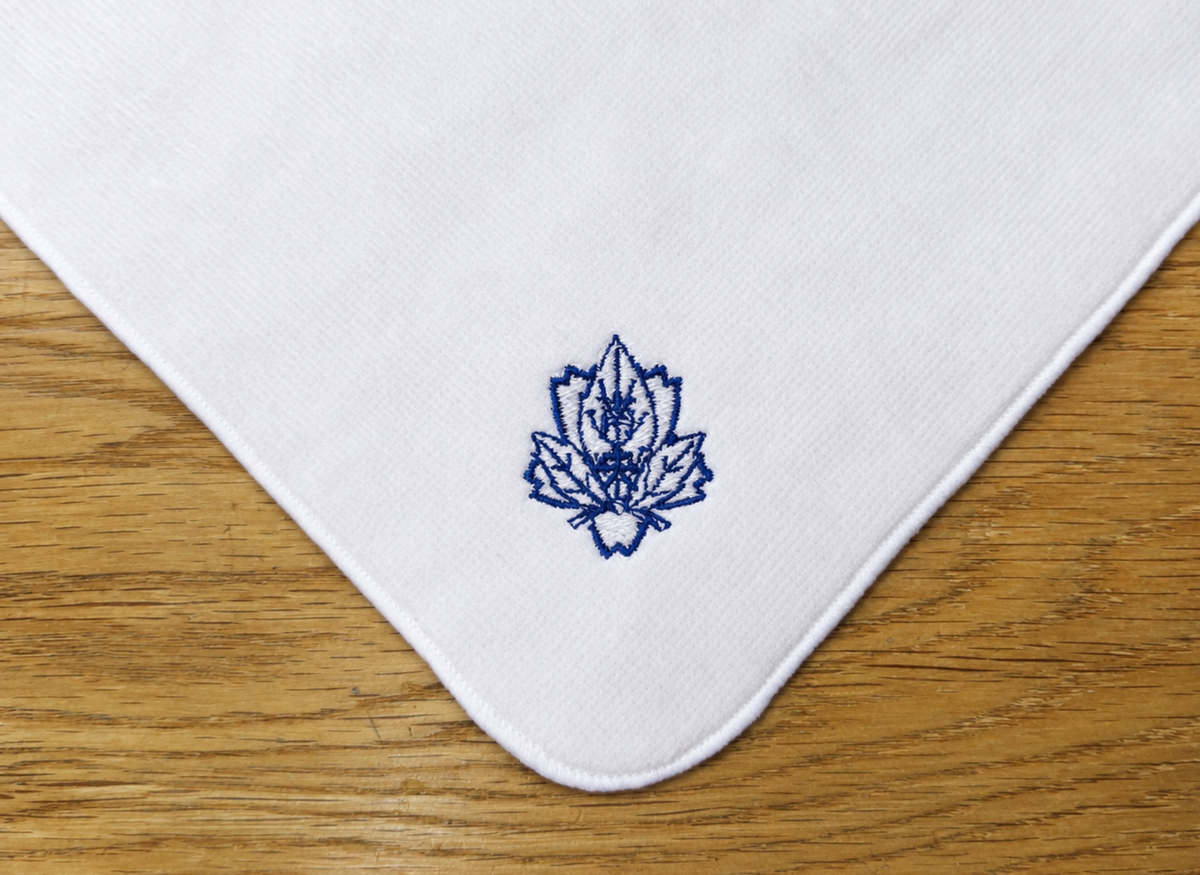 白いハンドタオルに紺色の糸で学校の校章を刺繍した卒業記念品の制作事例